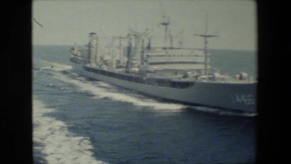 The white naval vessel continues through open water at an angle, with the hull number 146 partly visible, a broad wake trailing behind, and soft 8mm grain over the frame.