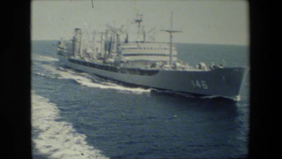 The vessel marked 146 moves through open ocean with its white bow and superstructure in view, leaving a bright wake under a pale sky in faded color 8mm footage.