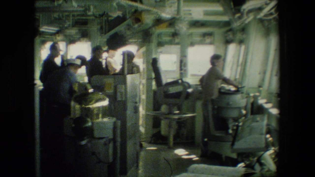 Uniformed sailors stand and work around shipboard control equipment inside a vessel.
