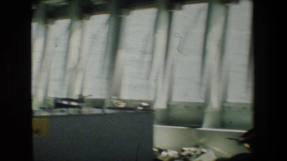 A handheld, motion-blurred frame shows vertical light-toned panels or windows above a low console inside the vessel interior.
