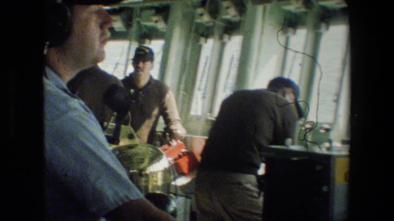 1981 8mm footage shows men inside a naval vessel workspace, with one man in headphones at left and others near consoles and equipment.