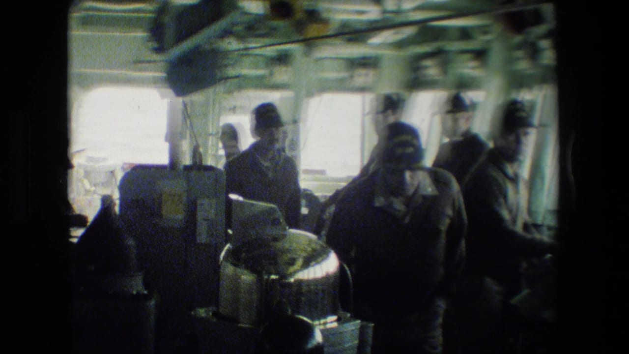 Uniformed men in caps move through the enclosed bridge of a military ship, with bright windows, overhead fittings, and control equipment visible in soft 8mm footage.
