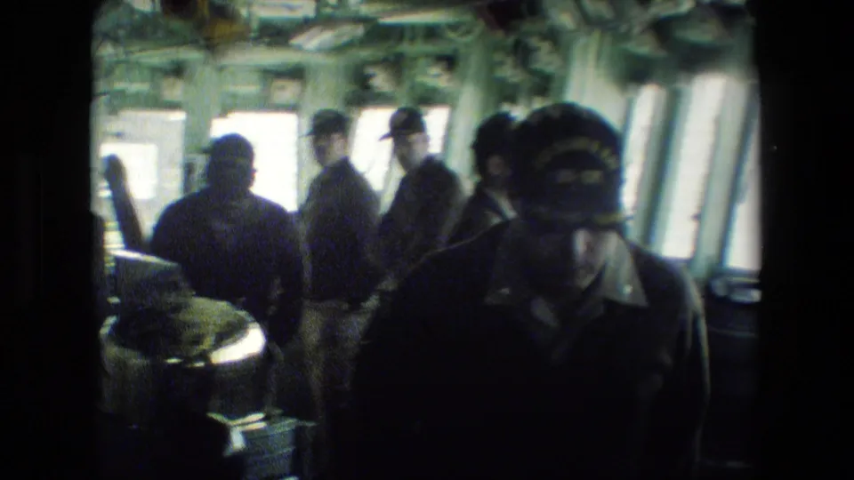 Several uniformed men appear inside the vessel bridge, partly silhouetted against bright windows, with shipboard fixtures and equipment surrounding them.