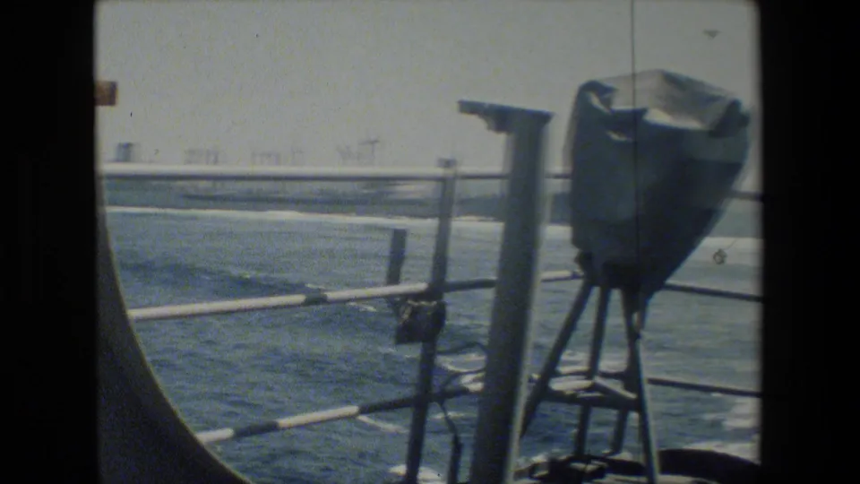 A later deck view shows the same railing line and mounted covered object with water beyond, filmed in faded color through soft 8mm exposure.