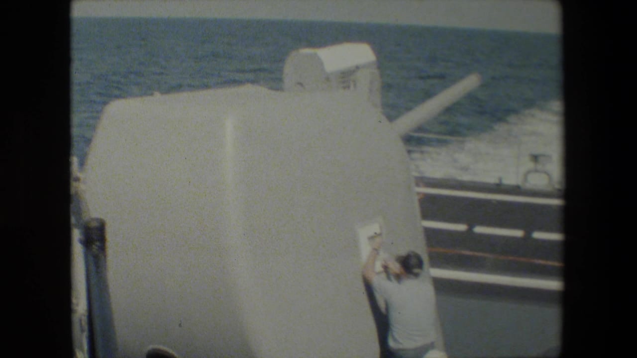 Large white gun turret on a ship deck with ocean wake behind it.