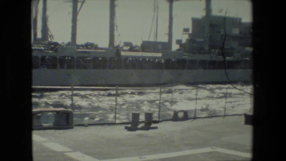 A faded 8mm frame shows a docked cargo-style ship beyond choppy water, with deck railings and small fittings in the foreground.