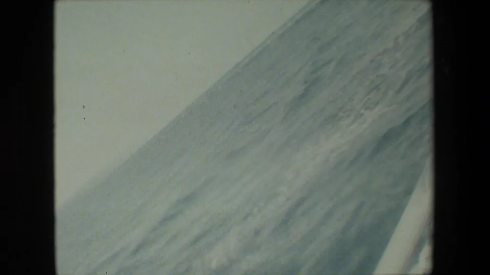 The frame shifts to a close, angled view of a pale vessel hull or deck surface, with faint texture and soft 8mm exposure.