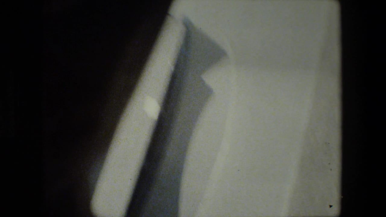 Opening 8mm frame with a dark contact-frame edge, a blurred light-toned foreground shape, and part of a gray docked vessel visible near the waterline.