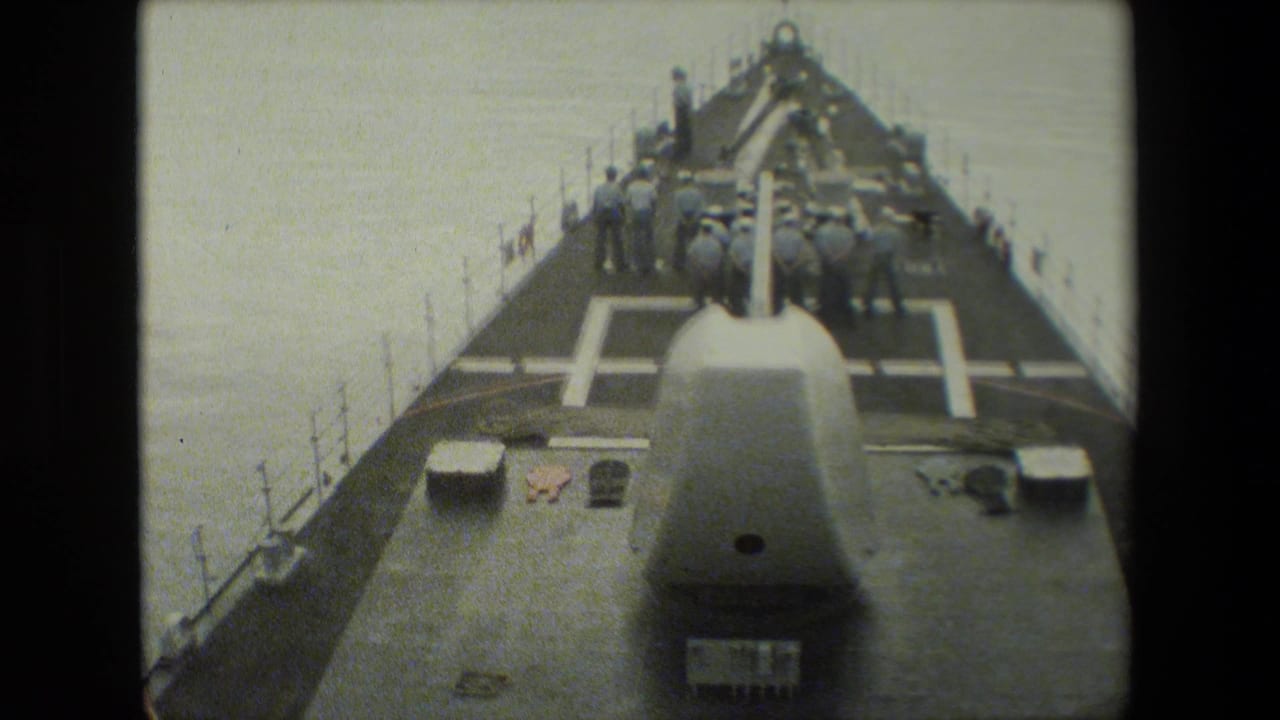 Naval ship bow with uniformed crewmen gathered near the forward deck equipment.