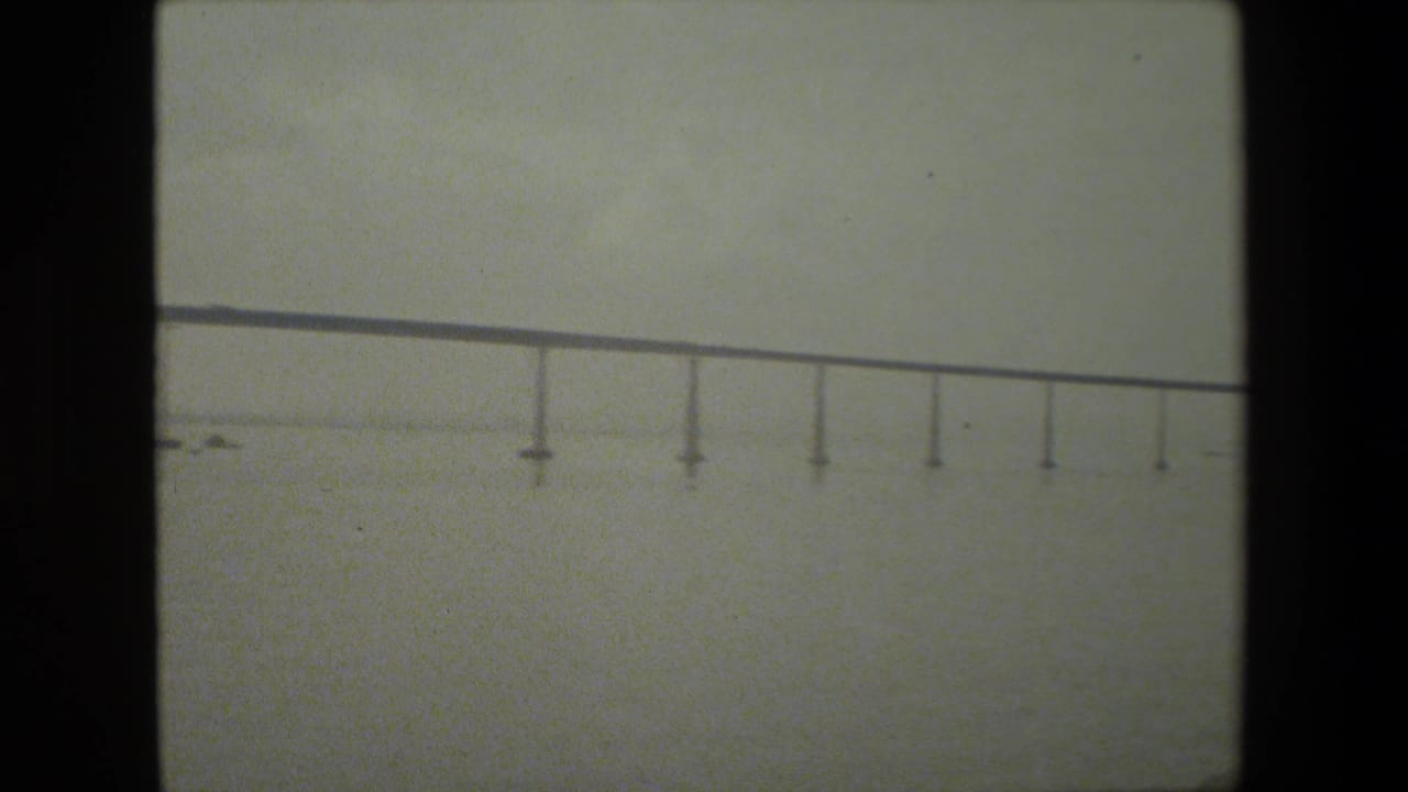 Long bridge deck with evenly spaced piers seen across open water.