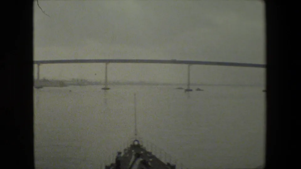 A bridge or elevated span crosses the upper frame above water, while a dark partial foreground shape enters at the bottom edge, consistent with a moving boat or vehicle viewpoint.