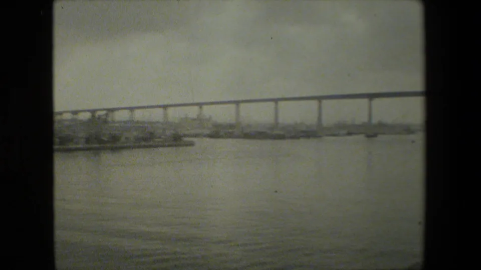 A wider boat perspective shows the bridge stretching across the upper frame, distant shoreline structures near the waterline, and rippled water in the foreground.