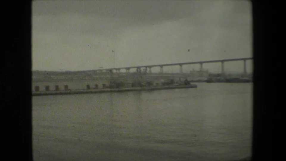 The final frame shows the bridge running across the background while pier pilings, shoreline structures, small boats, and calm water occupy the lower portion of the view.