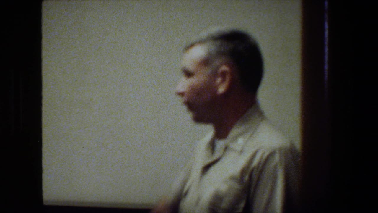 A blurred close view shows a uniformed man in profile against a plain ship interior wall, captured with handheld 8mm motion softness.