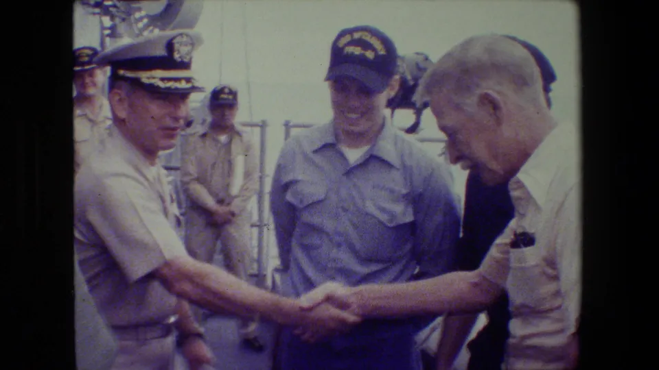 At the close of the clip, a uniformed officer and an older man appear to shake hands on the ship deck as other military personnel look on.