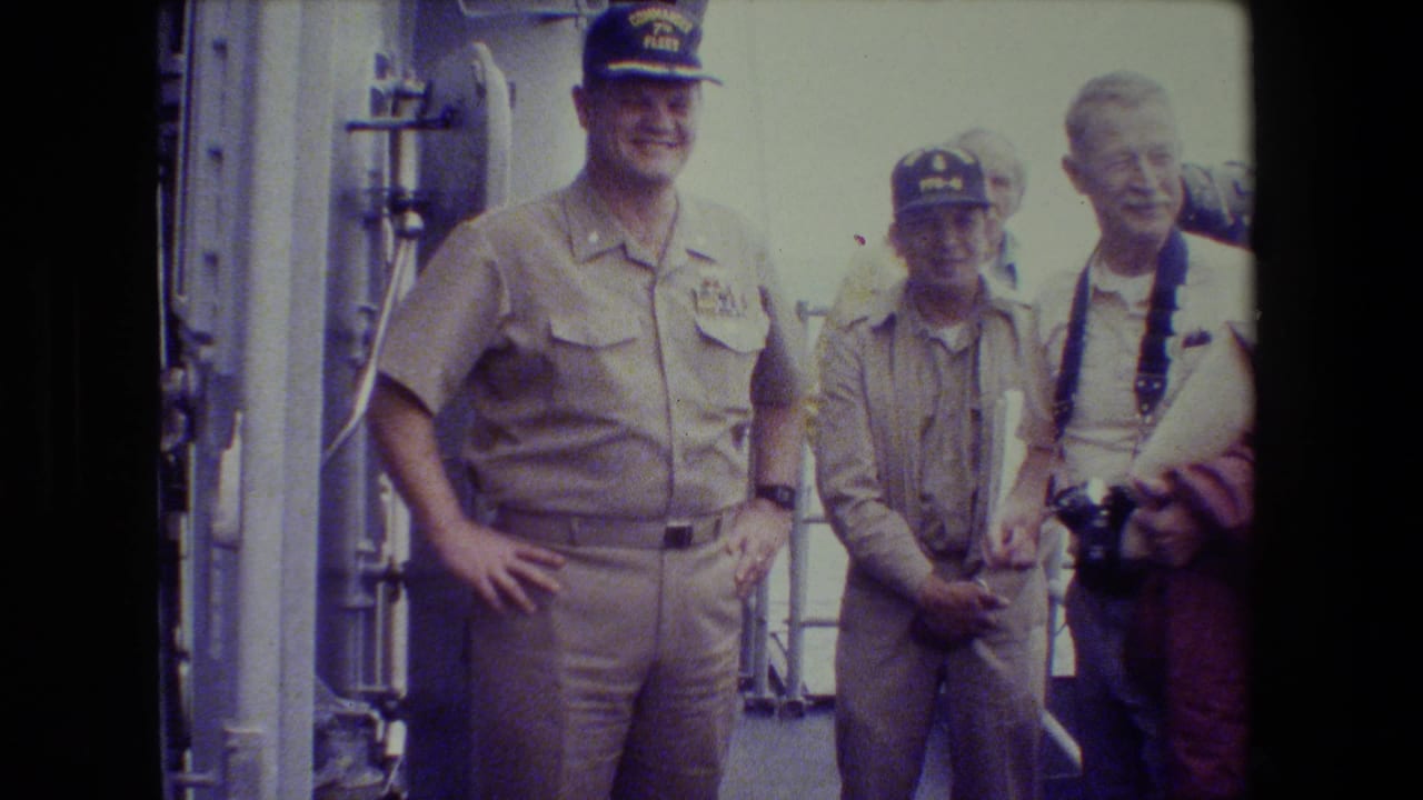 Two uniformed men pose near a smiling civilian with camera gear.