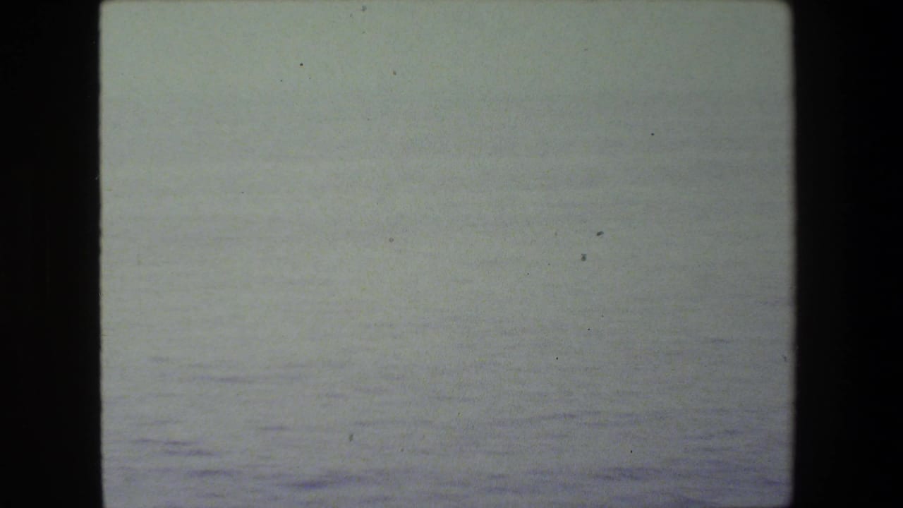 Soft, overexposed 8mm frame showing a pale ocean horizon or sea surface before the ship deck appears.