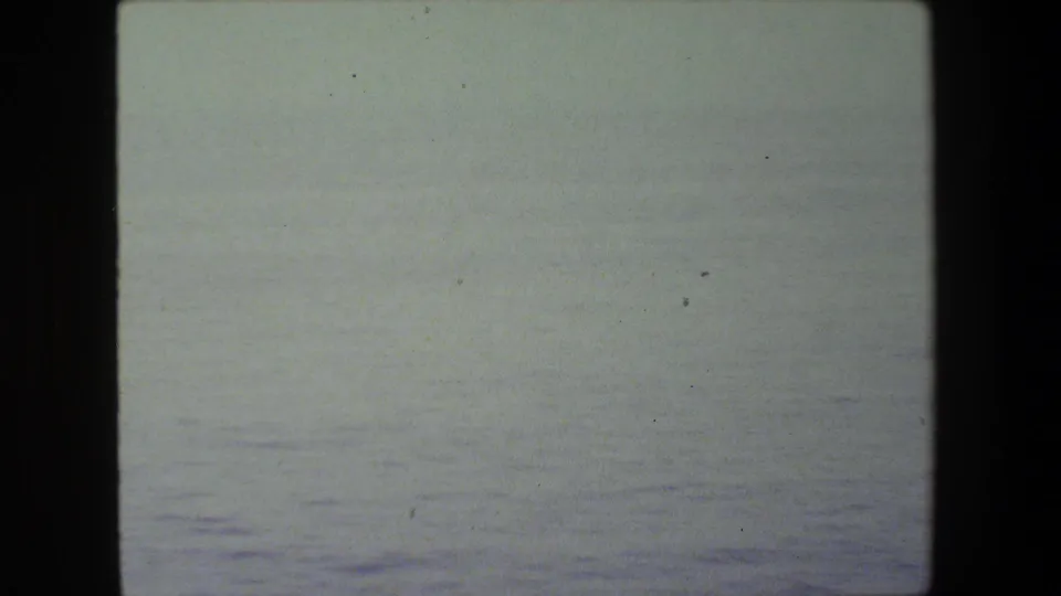 Soft, overexposed 8mm frame showing a pale ocean horizon or sea surface before the ship deck appears.