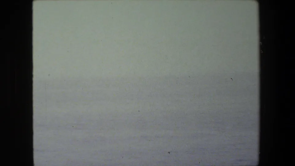 Faded 8mm frame of a bright, low-contrast sea view, functioning as a transition before the naval deck becomes visible.