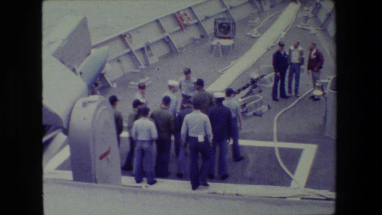 A group of men stands on a ship deck while several others face large deck equipment.