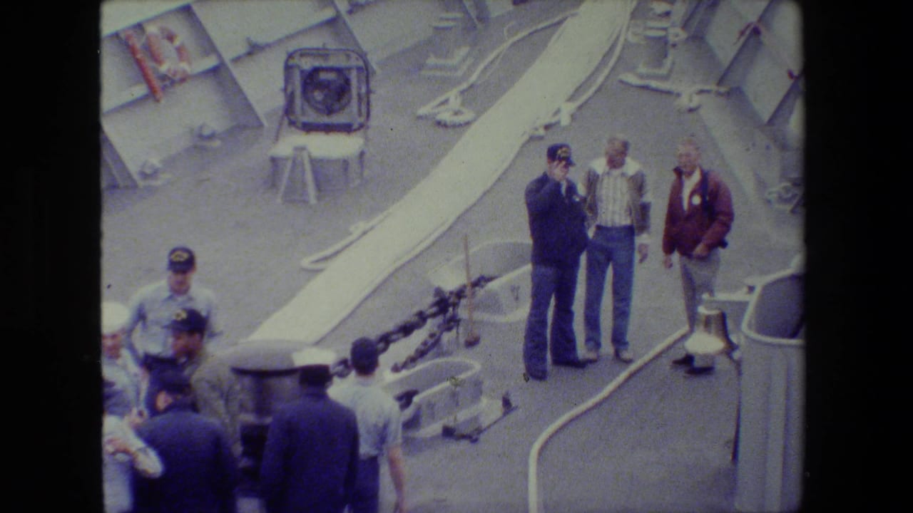 Men on a ship deck look outward near visible deck chains.