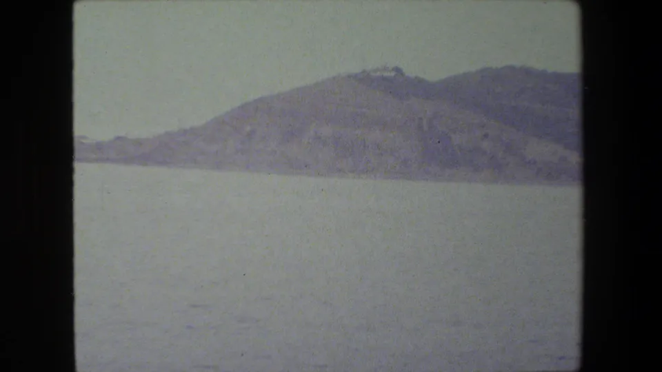 A broad view across open water shows a hazy shoreline or island in the distance, rendered in faded color from the 8mm home-movie scan.