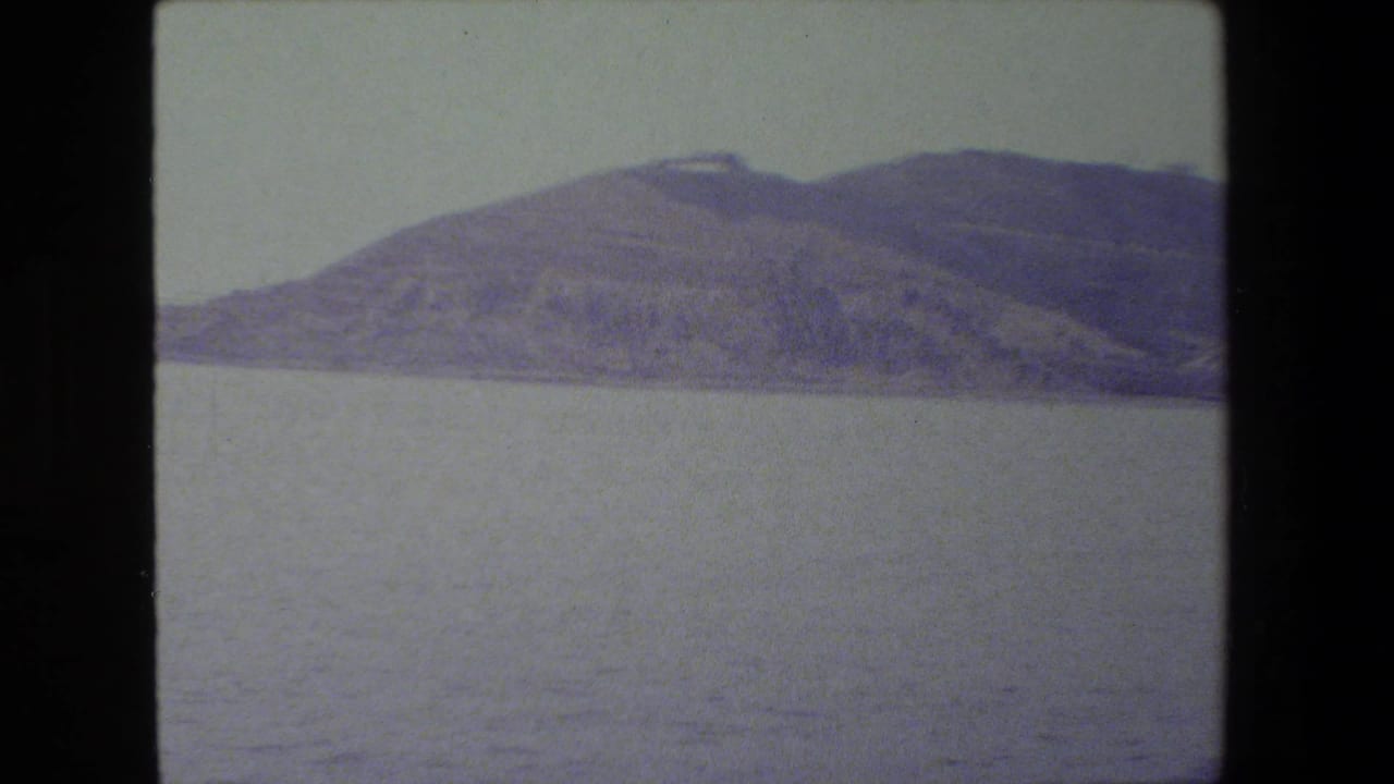 Soft 8mm frame showing calm open water and a distant hilly shoreline under a pale sky, with no visible people or vessels in this still.