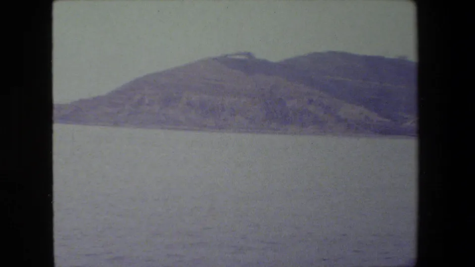 Soft 8mm frame showing calm open water and a distant hilly shoreline under a pale sky, with no visible people or vessels in this still.