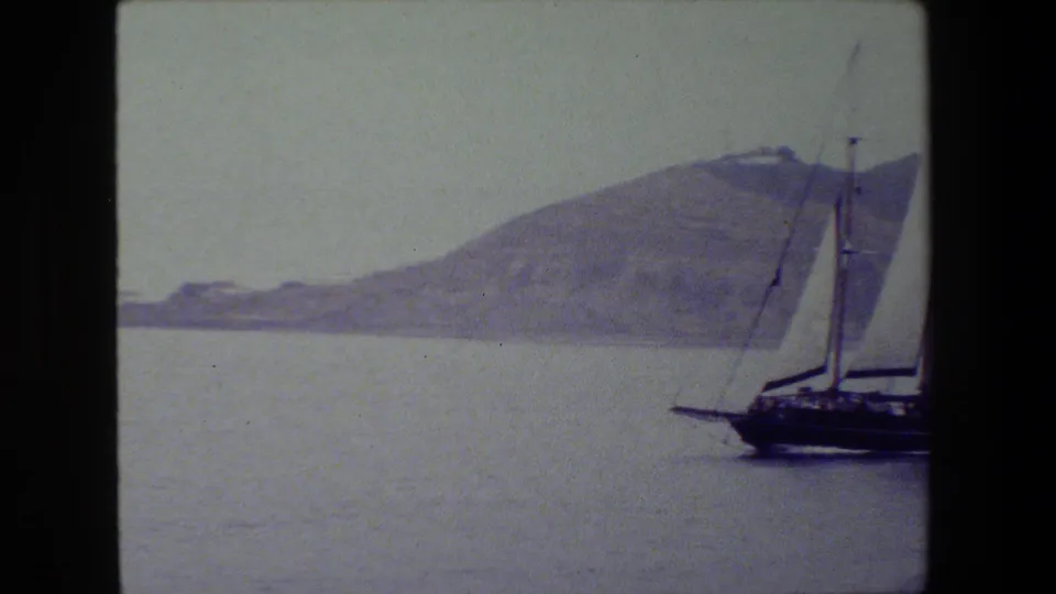 The sailboat is partly cropped at the right edge as it continues past the camera, leaving more open water and distant land visible.