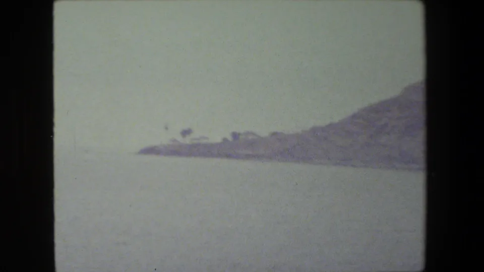 The final frame shows calm open water with a hazy strip of shoreline and hills, after the sailboat has moved out of view.