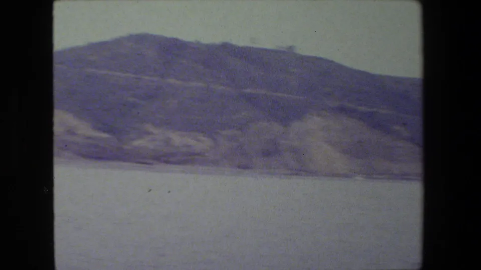The final frame shows the hillside continuing along the water, with dry landforms, a faint shoreline, and visible 8mm grain and color shift.