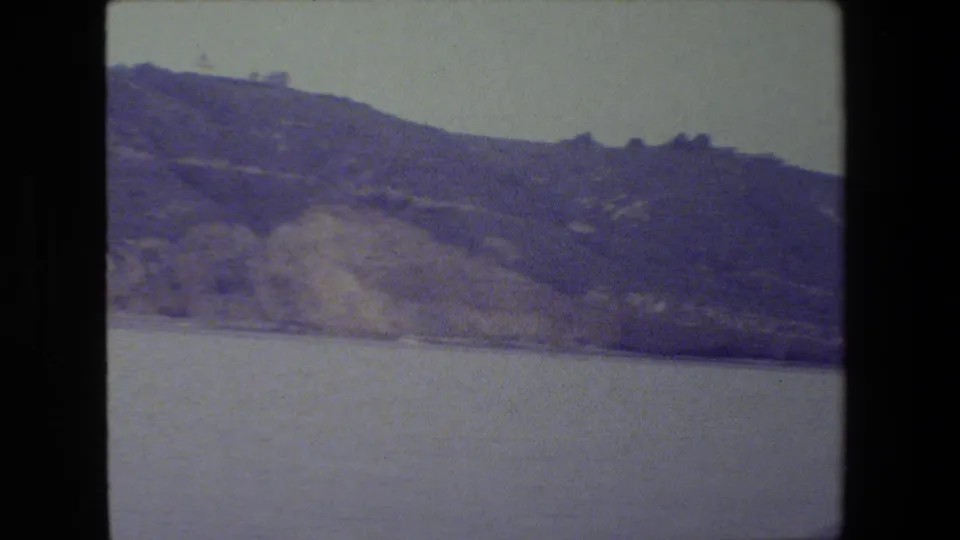 Soft 8mm view across calm water toward a low hilly shoreline, with no people or identifiable signs visible.