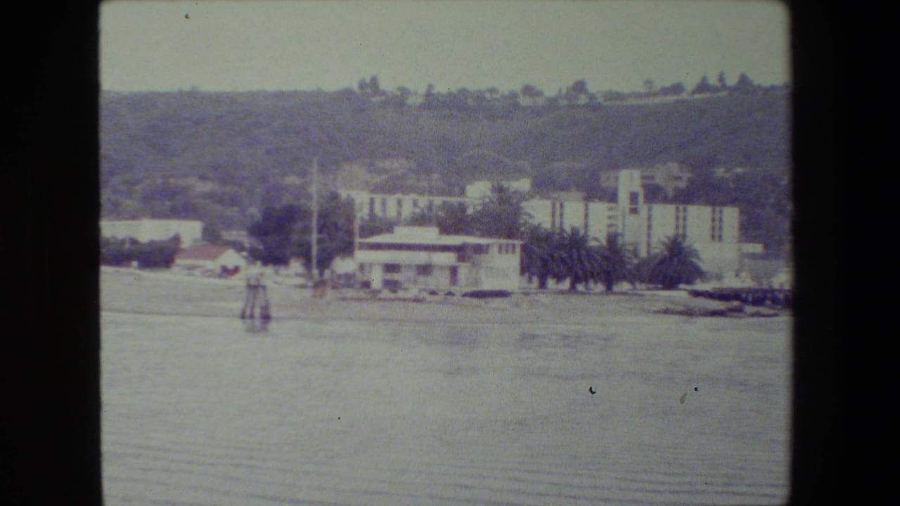 Waterfront buildings at the base of hills across calm water.