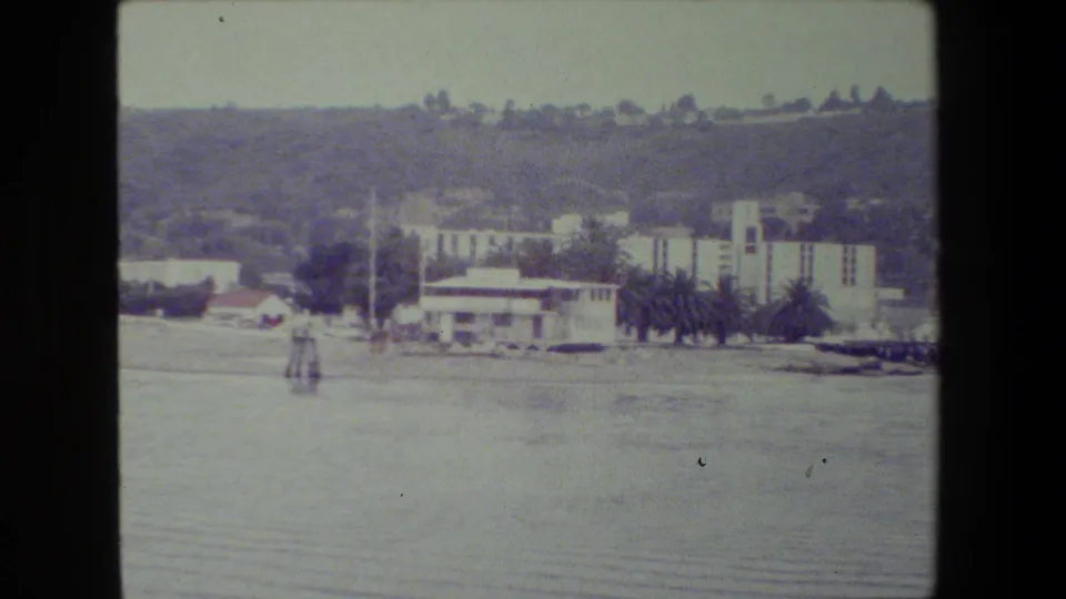 Distant waterfront buildings and trees appear below hills across calm harbor water, identified by supplied metadata as part of a San Diego naval-base view.