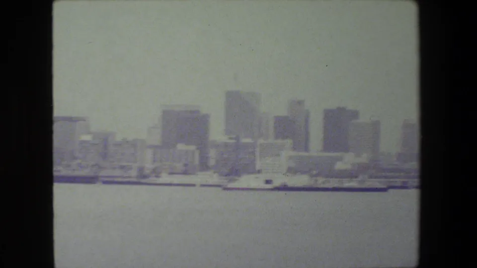 The camera frames open water and a hazy line of high-rise buildings along the waterfront, with the vessel mostly outside the visible frame.