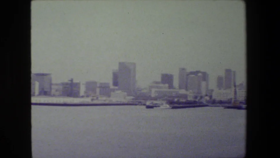 San Diego waterfront panorama from 1981 showing open harbor water, small vessels, docked ships, and a modern city skyline softened by 8mm film grain.