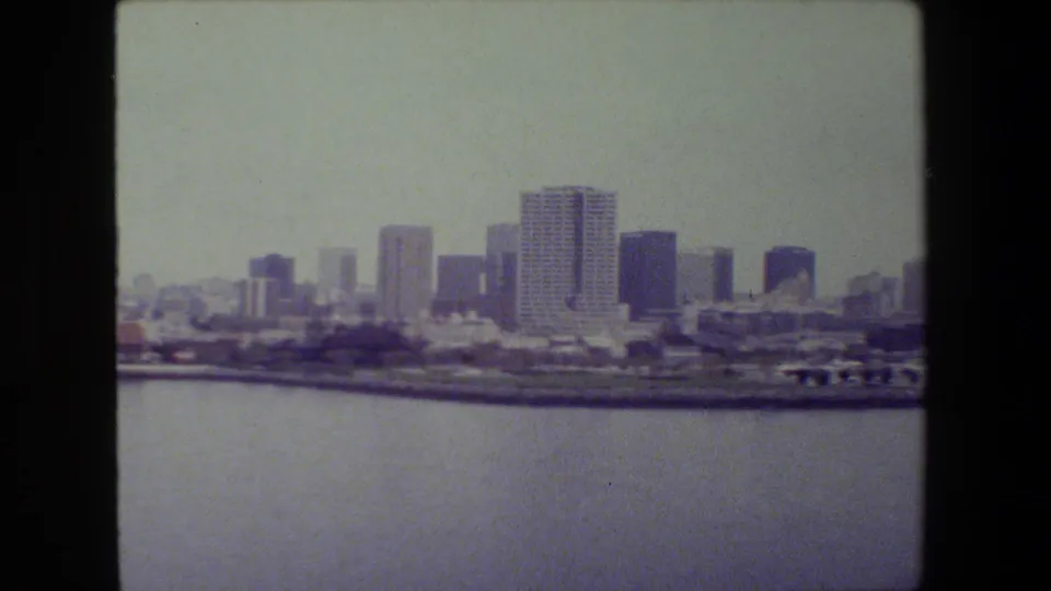 Final panoramic frame showing harbor water in front of a coastal skyline with high-rises, low shoreline buildings, and visible 8mm frame borders from the scanned home-movie source.