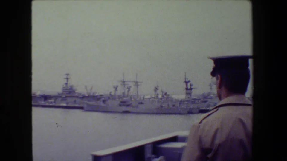 A uniformed naval officer stands in the foreground looking toward docked U.S. Navy ships at San Diego Naval Base in 1981.