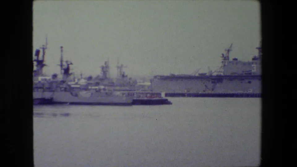 Several gray Navy vessels and pier structures line the harbor at San Diego Naval Base in a faded 1981 8mm frame.