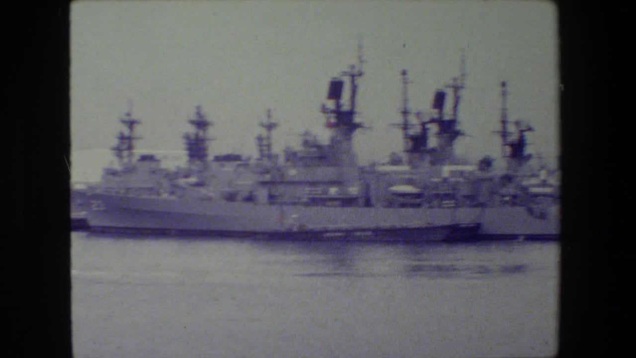 Large docked warship with several naval vessels behind it.