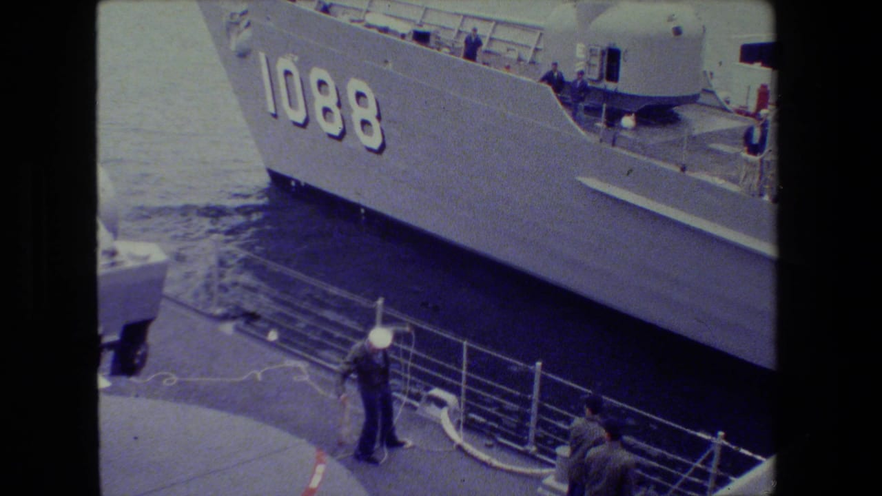 Gray naval ship marked 1088 beside sailors and mooring lines at a pier.