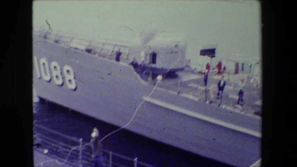 A gray naval ship marked 1088 is seen close to a pier as sailors on deck and below manage a line during a docking or mooring action.