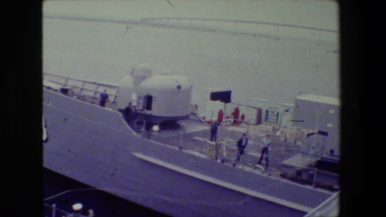 1981 archival 8mm frame showing adult men on the deck of a large naval vessel at the San Diego Naval Base, with the number 88 and a dome-shaped deck structure visible.