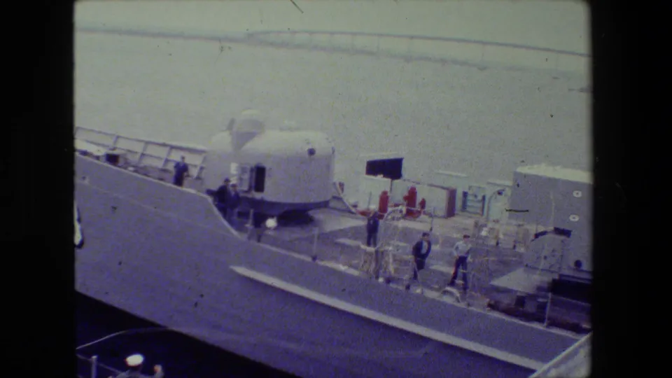 1981 archival 8mm frame showing adult men on the deck of a large naval vessel at the San Diego Naval Base, with the number 88 and a dome-shaped deck structure visible.