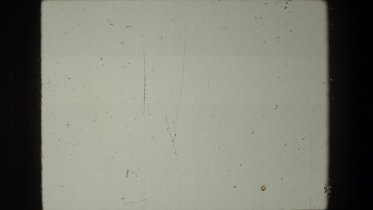 Mostly blank film frame with dust, scratches, and light exposure marks.