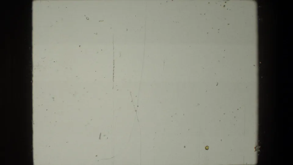 Mostly blank end-of-reel 8mm frame with pale exposure, visible dust specks, scratches, and no discernible people or location details.