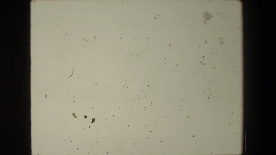 Blank end-of-reel 8mm frame with faded color, scattered dust, small scratches, and no identifiable subject matter.