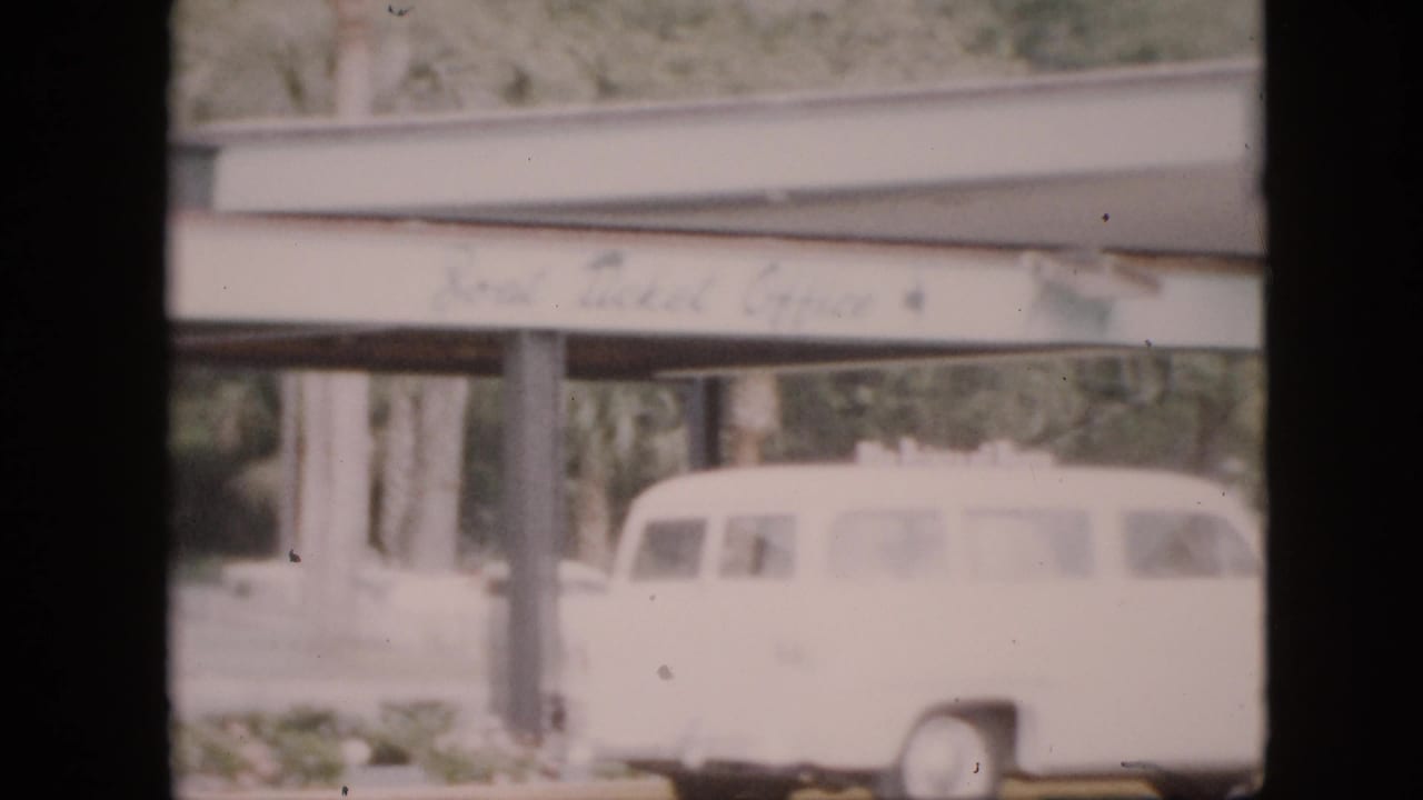 White station wagon below a covered campus structure, with signage and pillars in soft focus.