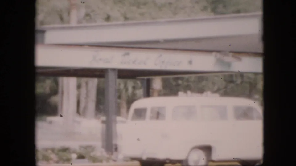 White station wagon, likely with wood side paneling, passes or sits below a covered structure on a 1958 Pennsylvania campus, with pillars and blurred signage above.