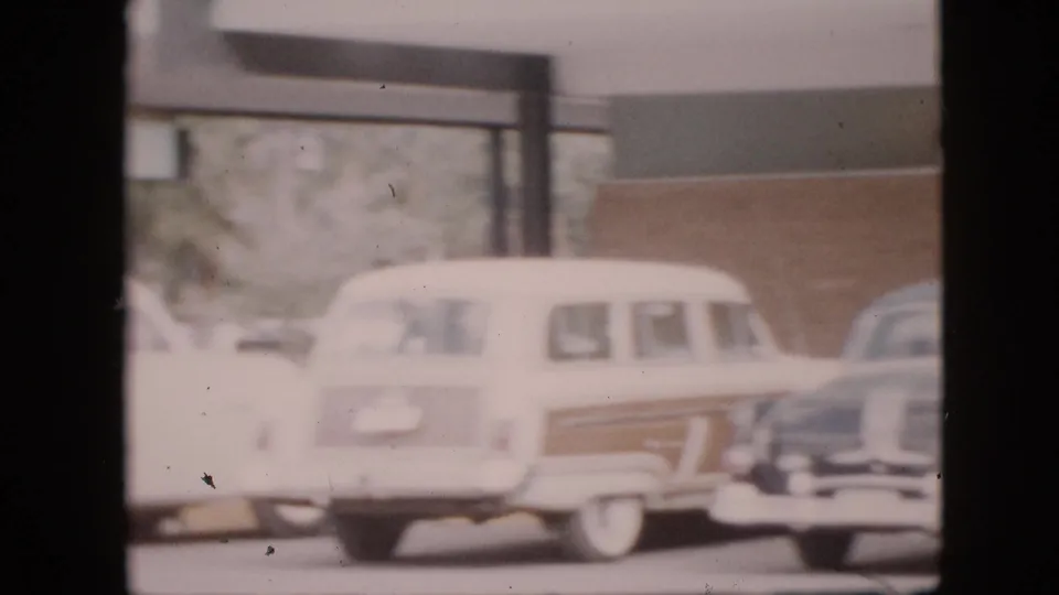 A white wood-paneled station wagon and neighboring parked cars are visible near a covered walkway on a 1958 Pennsylvania campus, framed by dark vertical edges.
